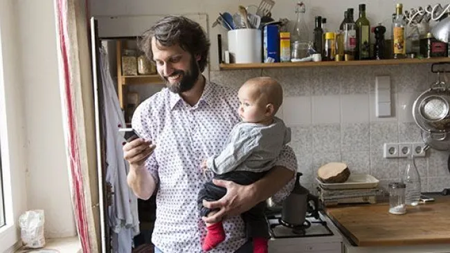 A man holding a baby while checking his phone