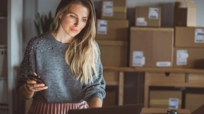 Woman holding her phone while checking her laptop