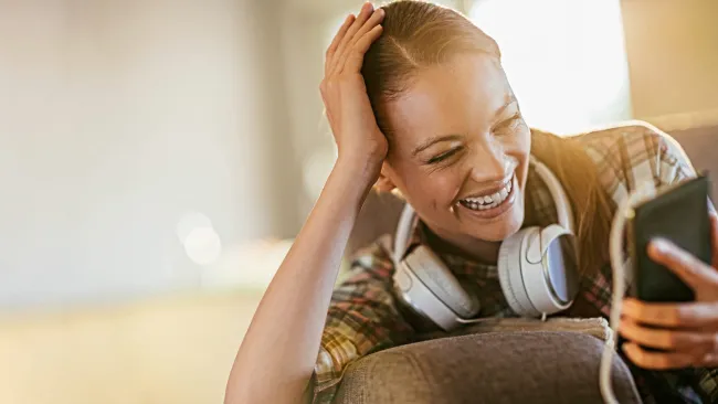 Smiling woman wearing headphones plugged into her phone