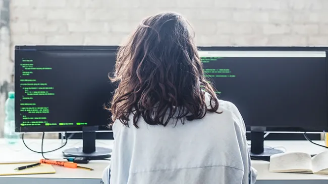 Woman working at a desk with two monitors