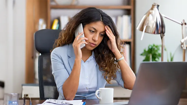 Frustrated woman holding a smartphone and looking at her laptop