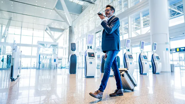 Man walking through an airport rolling luggage and talking on a cellphone