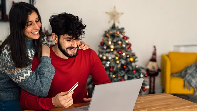 Man and woman looking at a laptop, holding a credit card, with a Christmas tree in the background