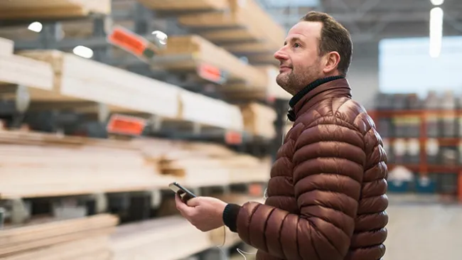Man holding cellphone while looking at lumber in a home improvement store