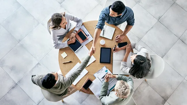 A group of coworkers sitting at a table, two of whom are shaking hands