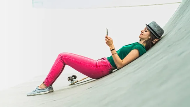 Woman using her phone while sitting near a skateboard