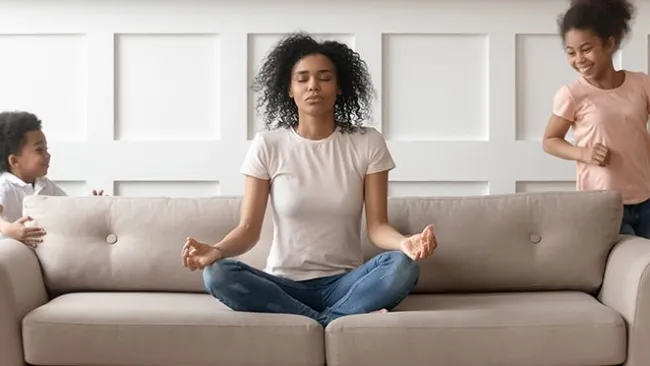 Mother in a yoga pose on a couch surrounded by her children