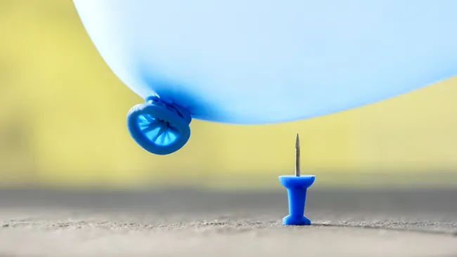 A blue balloon about to pop on a thumbtack