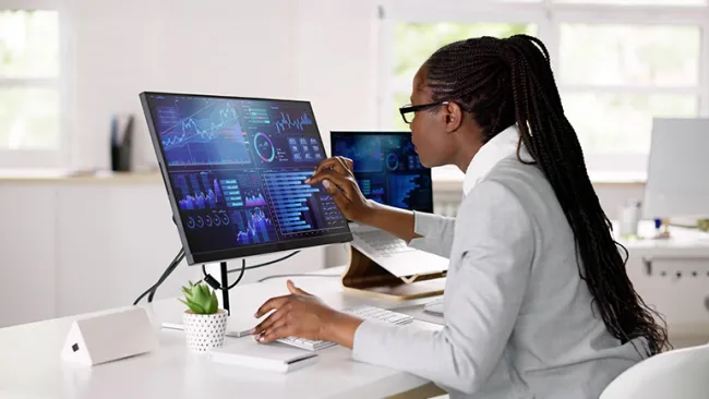 A woman looking and pointing at a computer screen showing charts and graphs