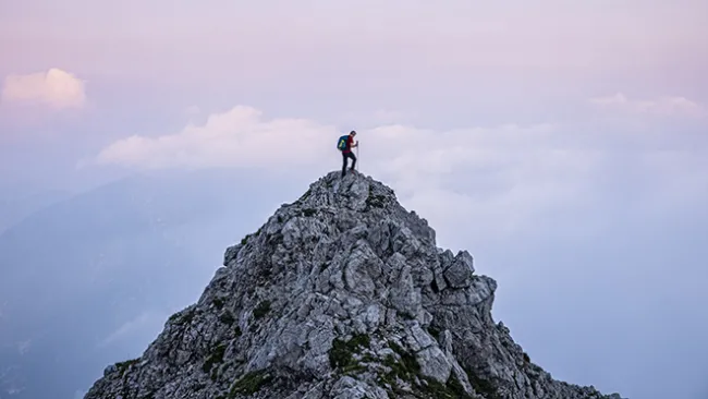 Person in hiking/climbing gear standing at the top of a mountain peak