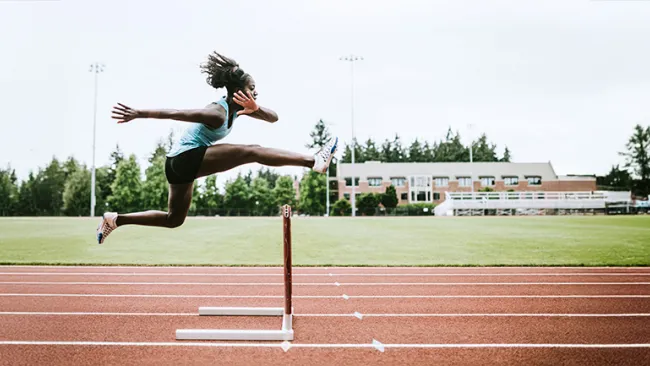 Woman on a track jumping over a hurdle