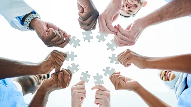 A circle of many people's hands, each holding a puzzle piece 