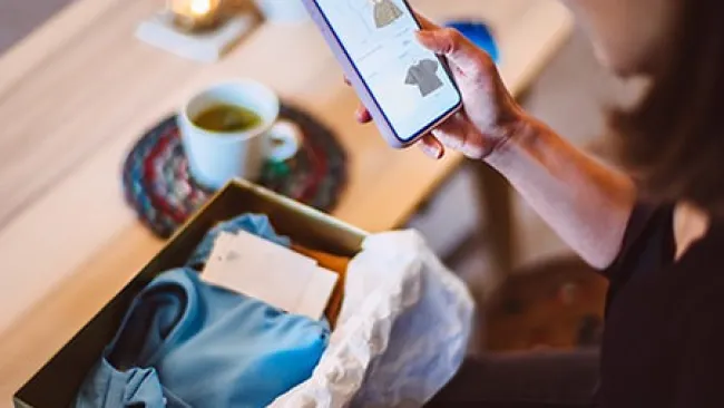 Woman looking at a retail website on her phone with a package in front of her