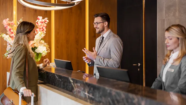 Woman checking in to a hotel with two hotel employees at the front desk