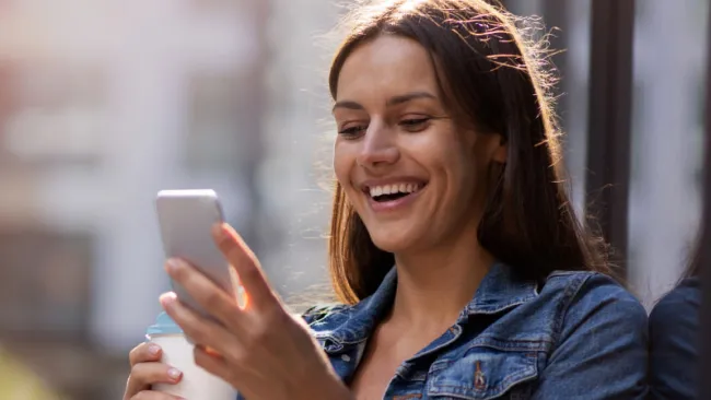 Smiling woman holding a coffee cup in one hand and her phone in the other