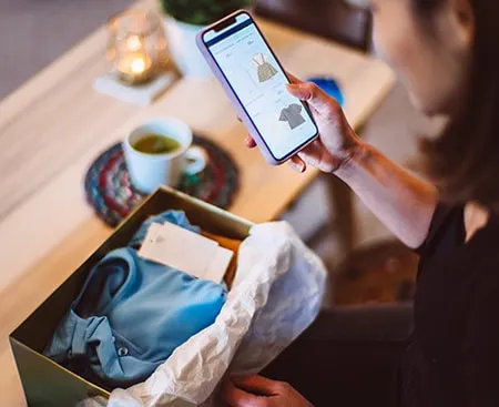 Woman looking at a retail website on her phone with a package in front of her