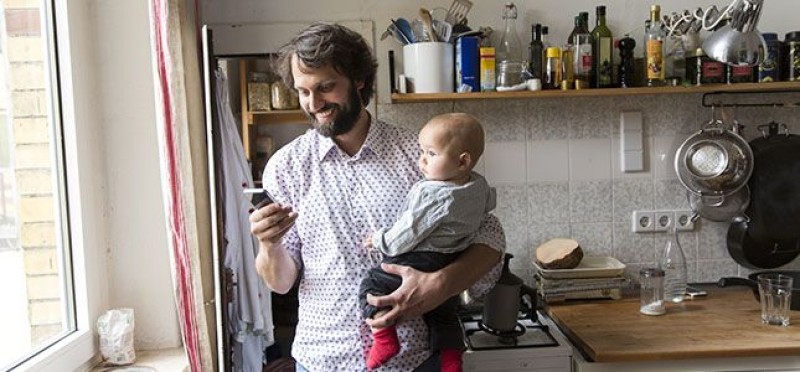 A man holding a baby while checking his phone