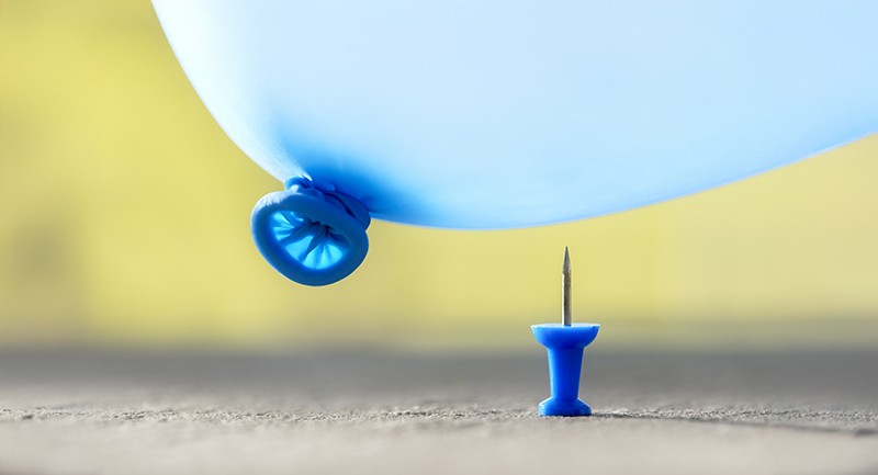 A blue balloon about to pop on a thumbtack