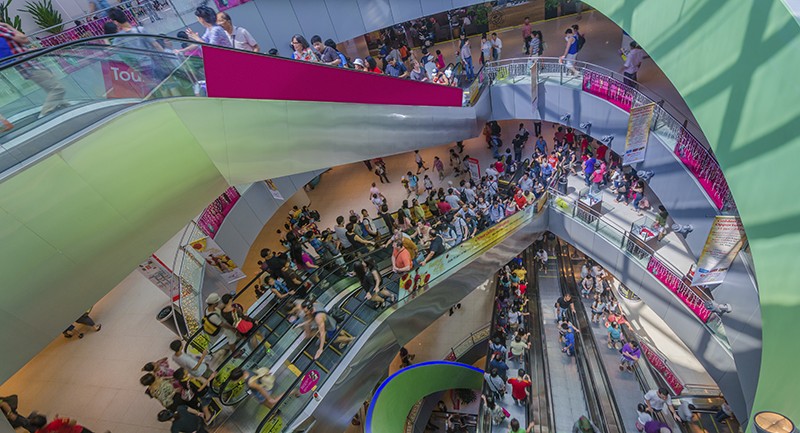 Spiral escalator full of shoppers at a busy mall 