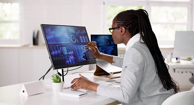 A woman looking and pointing at a computer screen showing charts and graphs