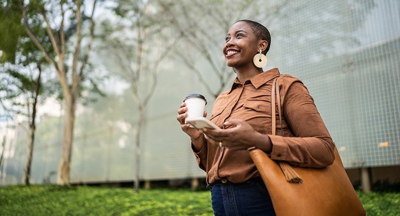 Woman smiling, holding a coffee in one hand and a smartphone in the other