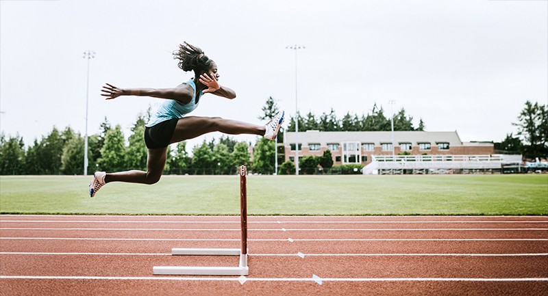 Woman on a track jumping over a hurdle