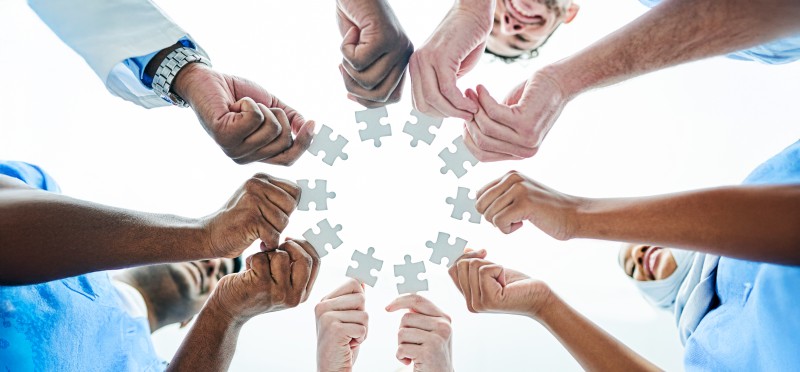 A circle of many people's hands, each holding a puzzle piece 