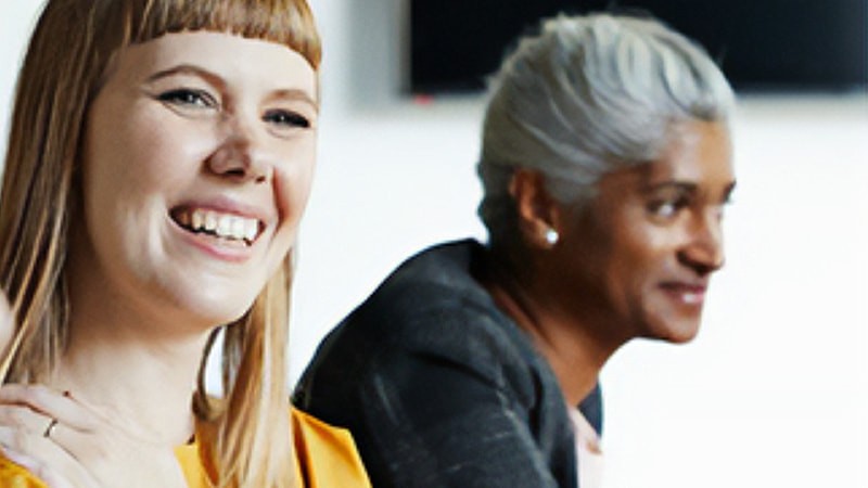 Woman smiling towards the camera with a man sitting next to her