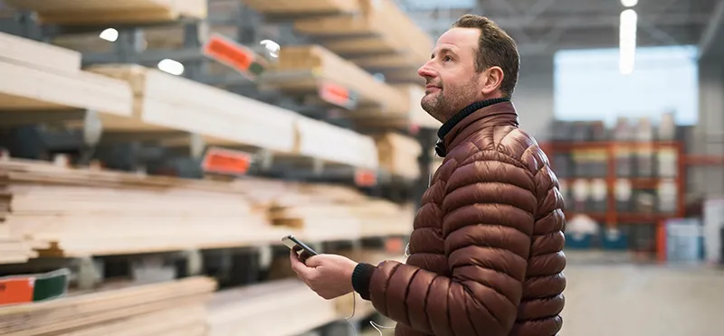 Man holding cellphone while looking at lumber in a home improvement store