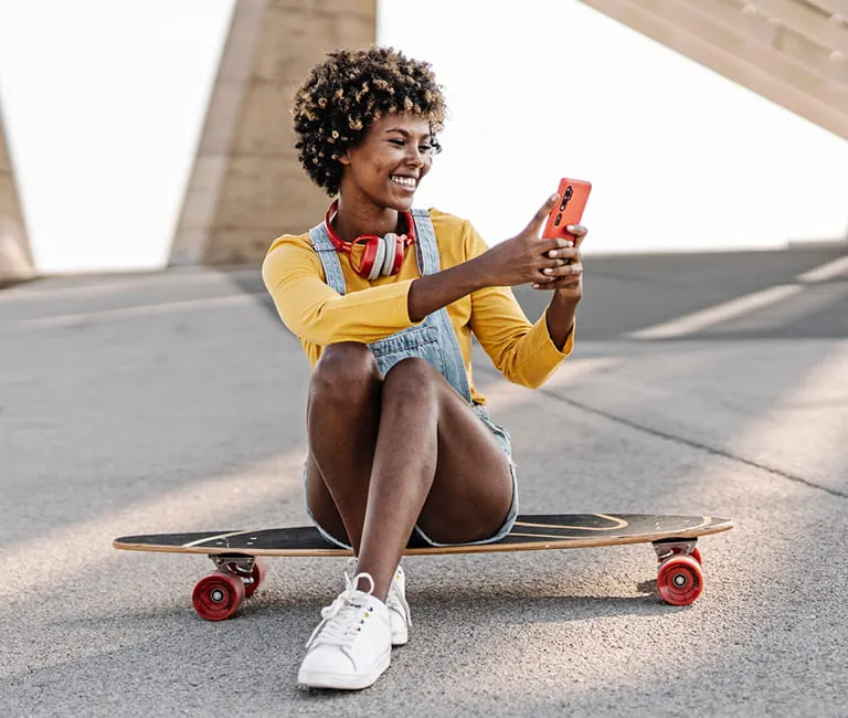 Woman using her phone while sitting on skateboard
