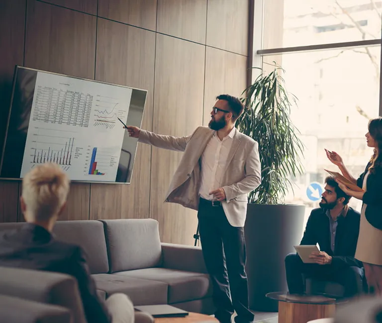 Man presenting charts on a television to a group in a conference room